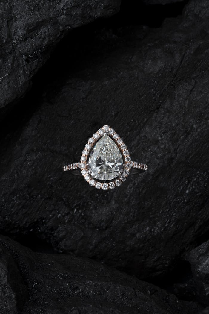 our-services-1 Stunning teardrop diamond ring surrounded by smaller stones on a textured dark background.