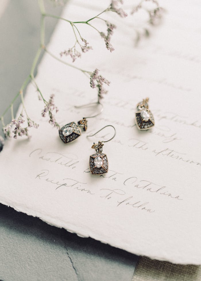 gallery-4 Close-up of elegant vintage earrings on a handwritten note adorned with delicate dried flowers.