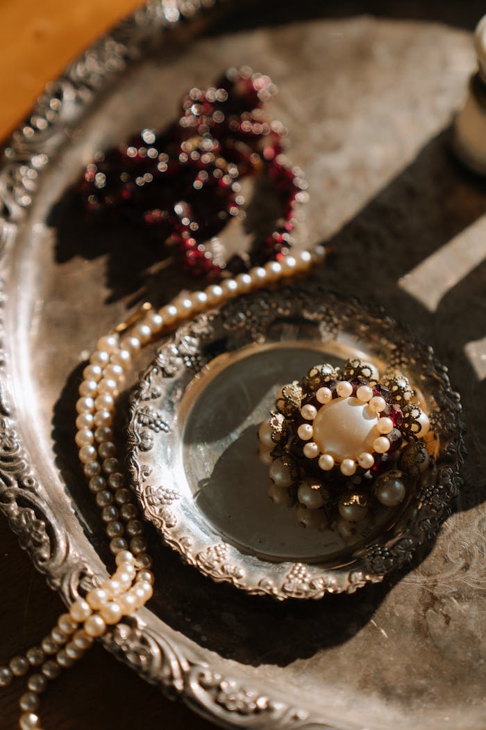gallery-3 Capture of a vintage silver tray adorned with pearls and intricate brooch, exuding elegance and classic style.
