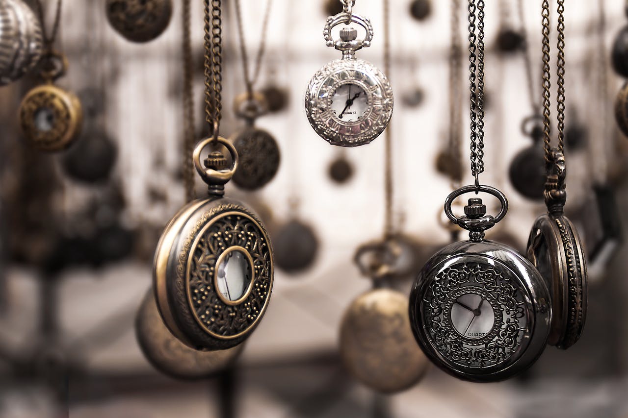 gallery-1 Close-up of antique pocket watches with intricate designs hanging in a blurred vintage setting.